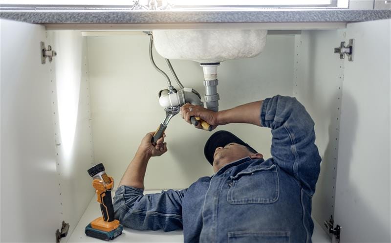 Plumber repairing pipes beneath a bathroom sink in Navarre