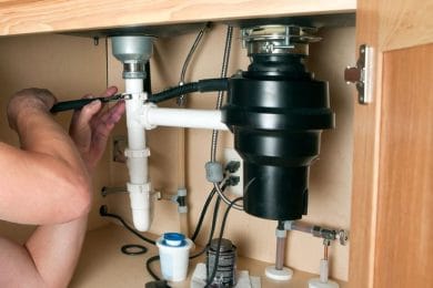 Plumber repairing a garbage disposal beneath a kitchen sink in Navarre
