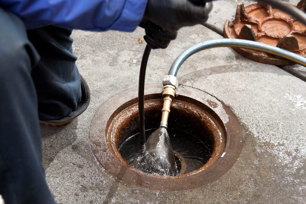 Plumber hydro jetting a sewer line through a manhole in Navarre